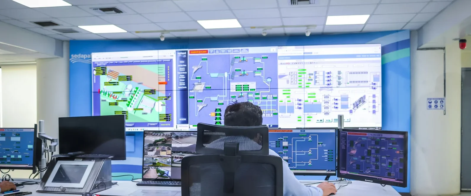 Operator monitoring industrial control systems and SCADA dashboards in a control room.