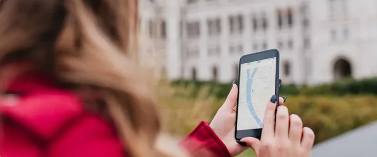 Woman in a red jacket using a smartphone to view a map outdoors in an urban setting.