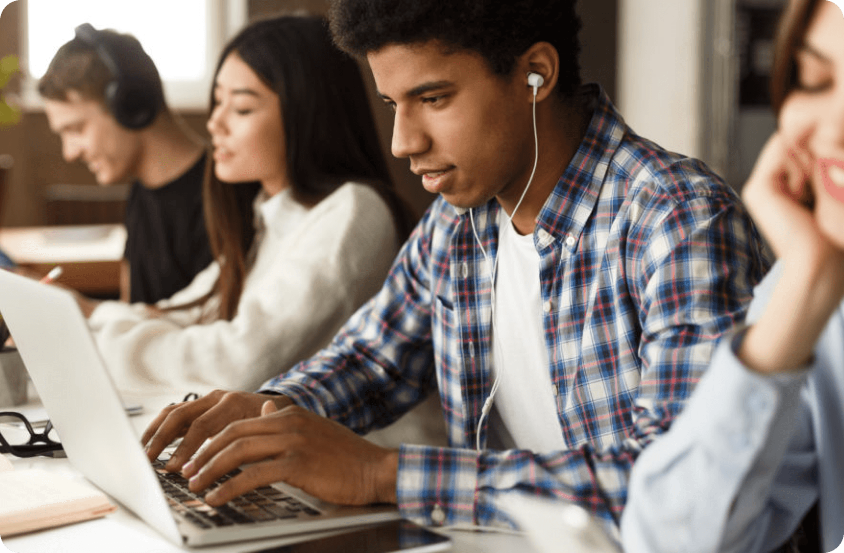 Diversos alunos estudando juntos com laptops e fones de ouvido em um ambiente de trabalho bem iluminado.