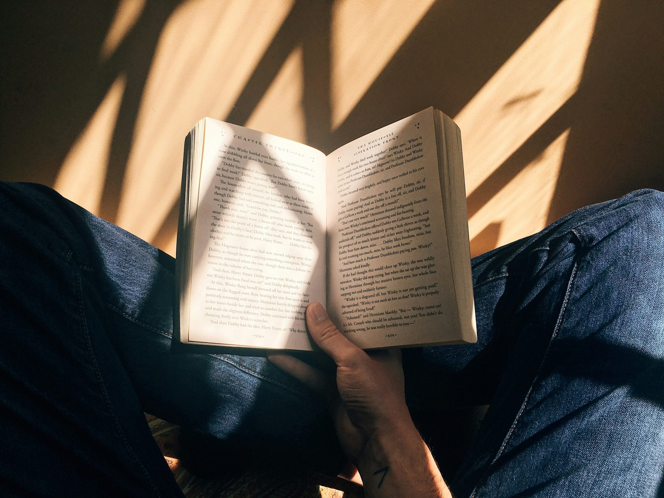 A person sitting on a chair, engrossed in an open book, captivated by the words on its pages.