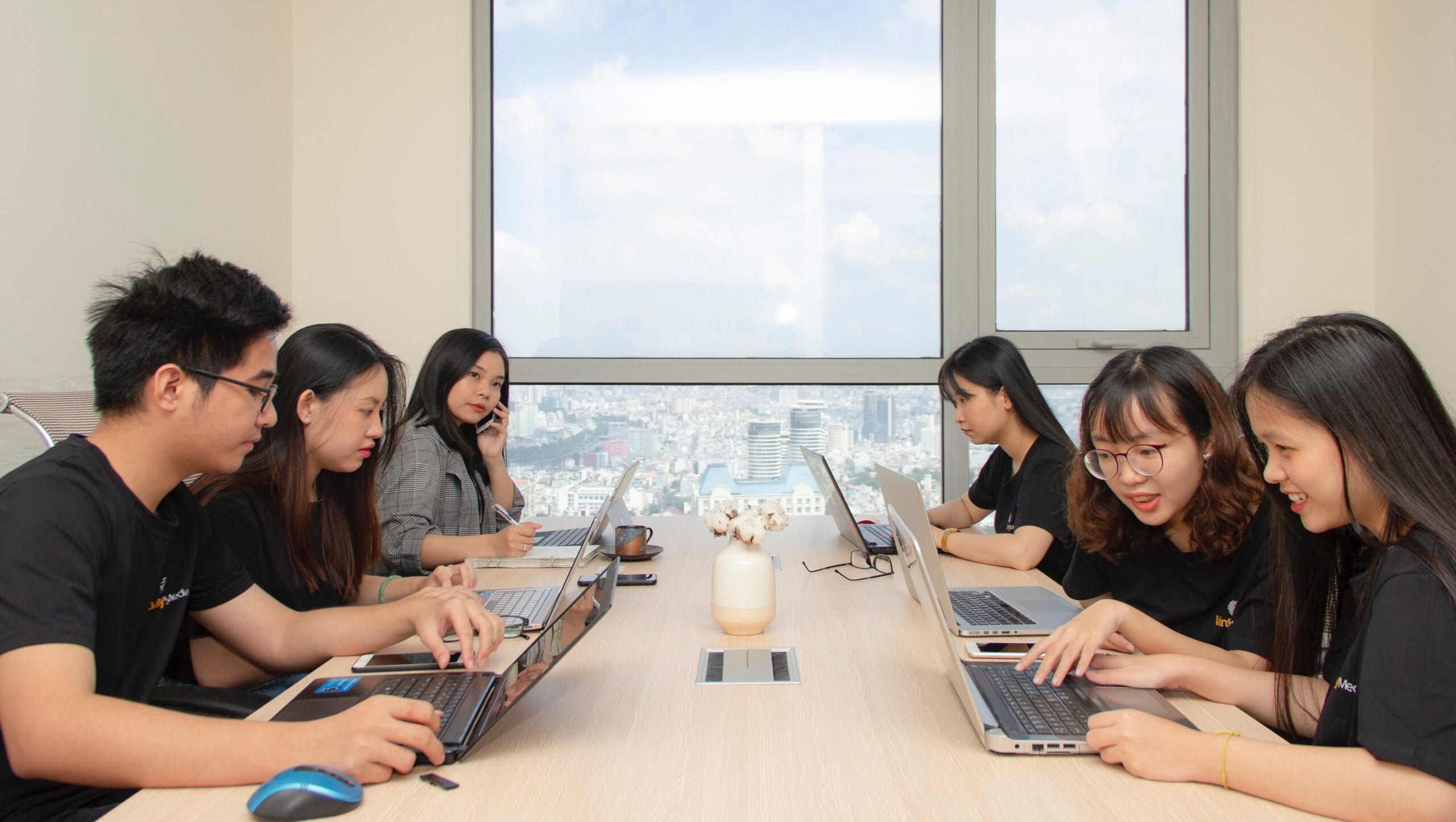 Six people sitting at table using laptops