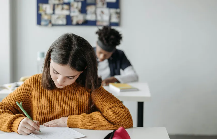 Student in knitted sweater writing in her notebook - the ADA Title II web accessibility rule in public education