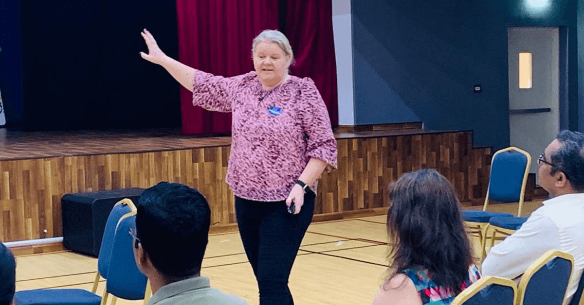 A woman standing on stage in front of an audience, giving a presentation.