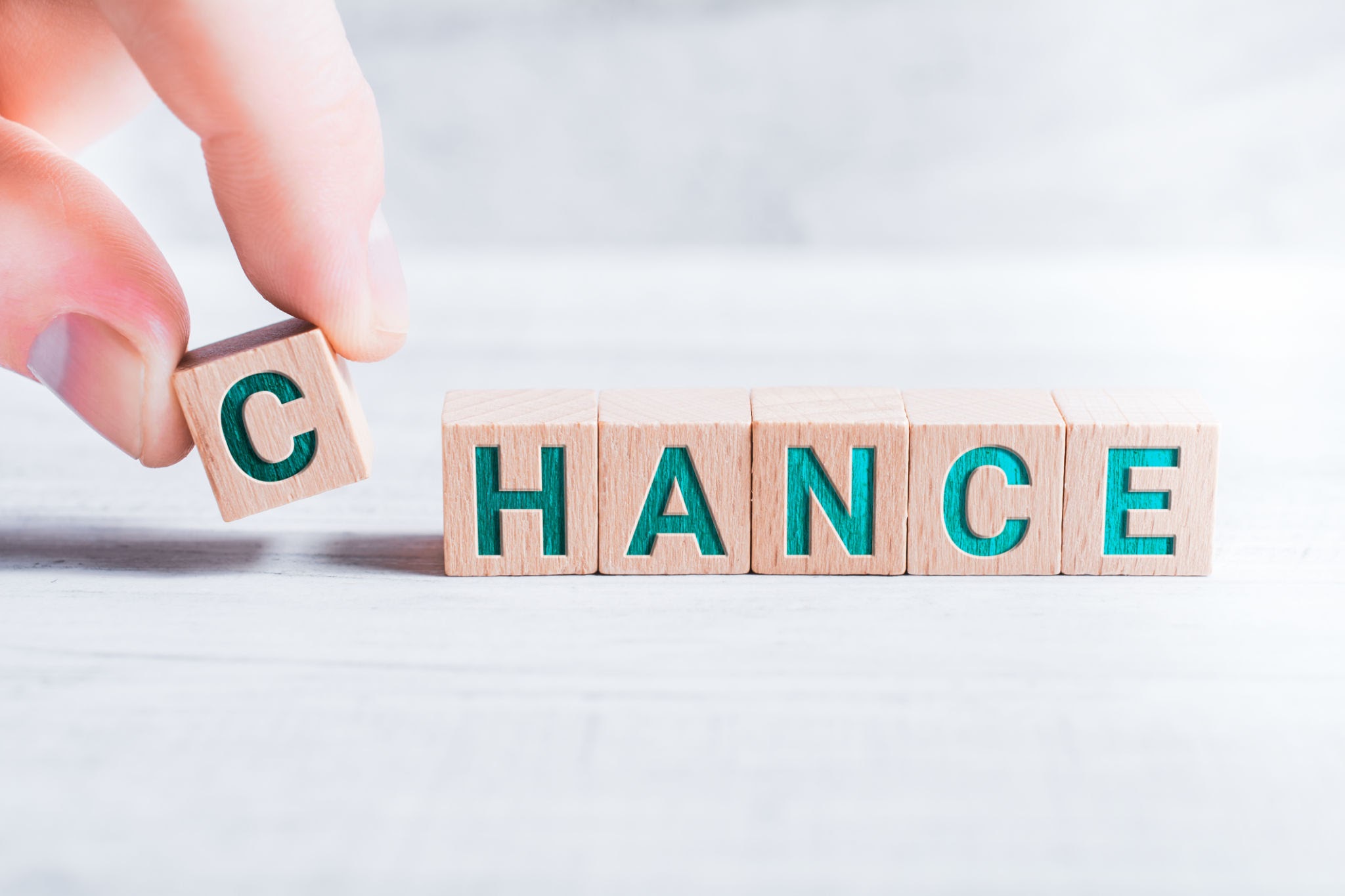 The Word Chance Formed By Wooden Blocks And Arranged By Male Fingers On White Table