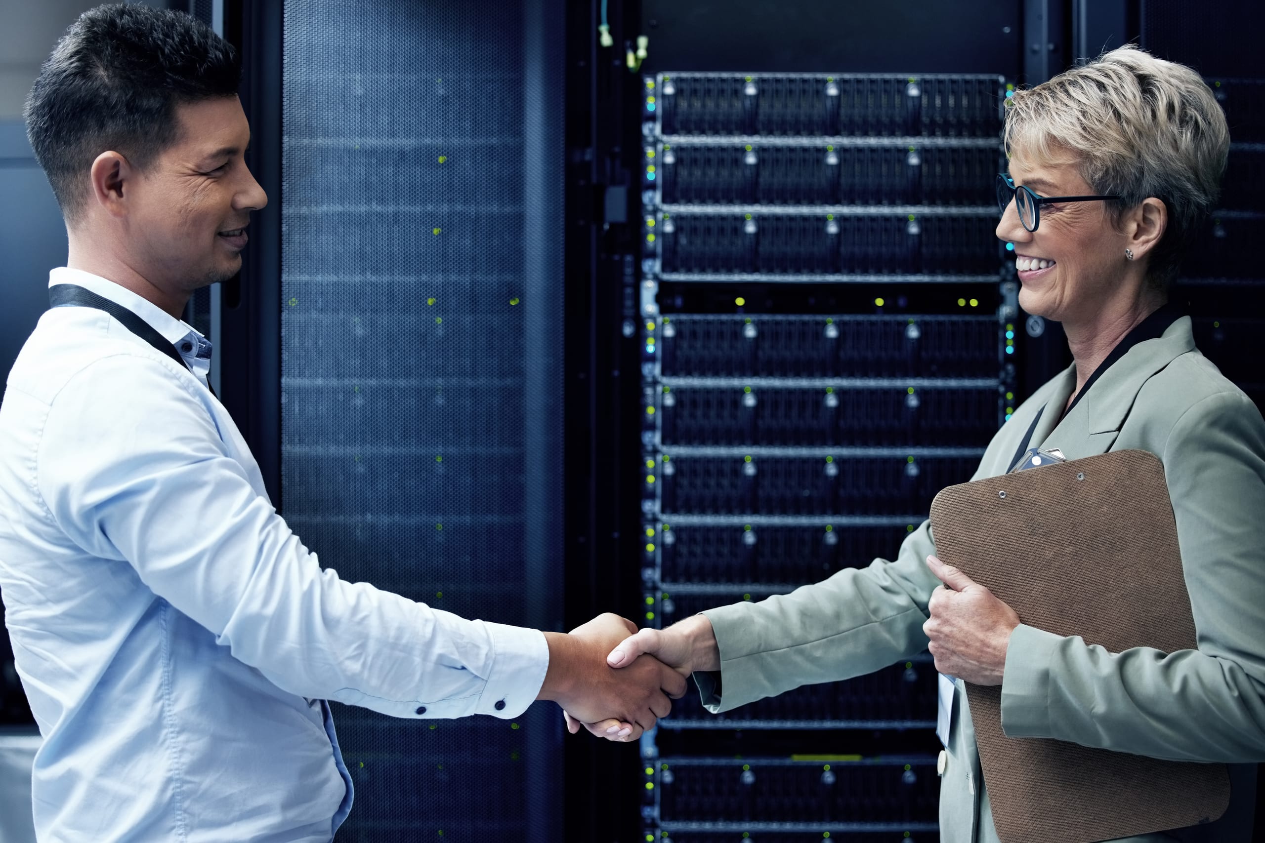 Two technicians shaking hands while working together in a server room.