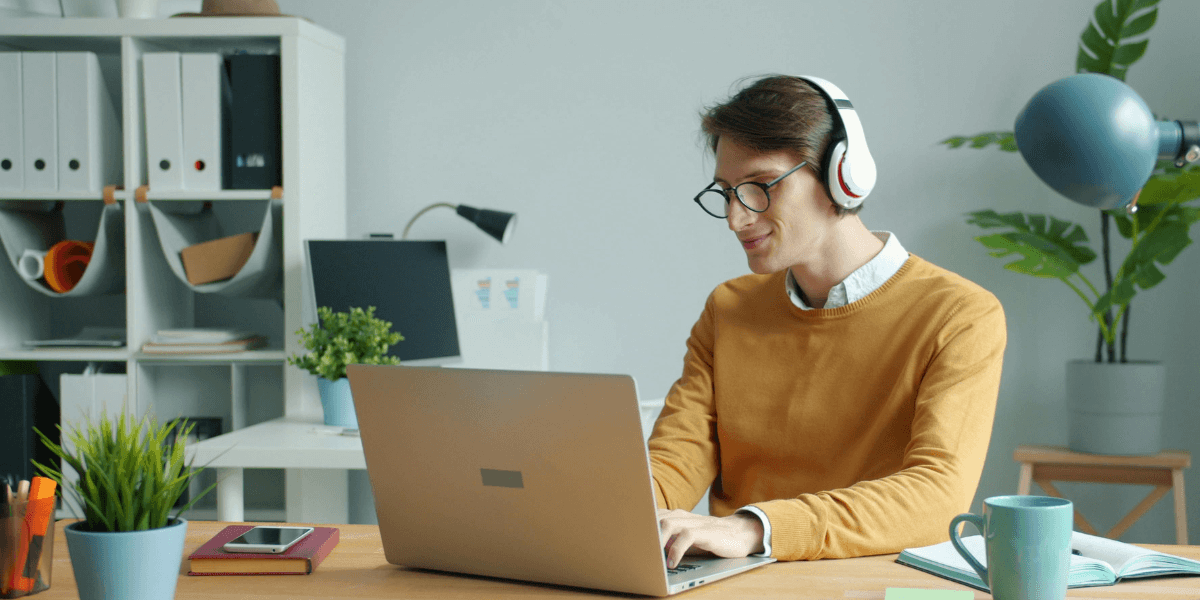 Young man with dark hair and glasses sitting in front of a laptop, and wearing headphones.