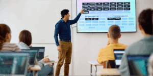 A teacher explains something to a blackboard in front of his class.