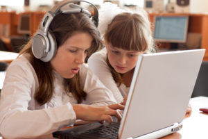 Twee leerlingen aan een laptop waarvan eentje luistert naar een tekst terwijl het wordt voorgelezen.