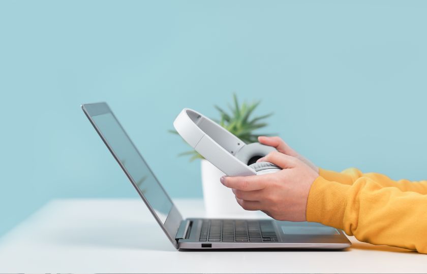 Un apprenant assis devant son ordinateur portable, avec un casque entre les mains.
