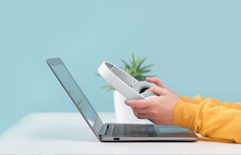 Lernende Person am Laptop mit Kopfhörer in den Händen.