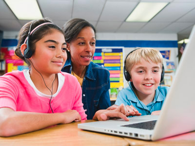 Teacher with two kids with headphones in front of a laptop